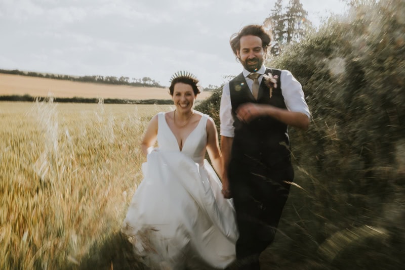 Kent Wedding Photographer, Husband and wife run through dry grass smiling at Symondsbury Estate, Dorset